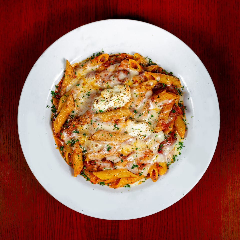 Baked penne pasta with melted mozzarella and ricotta cheese, topped with parsley, on a white plate.