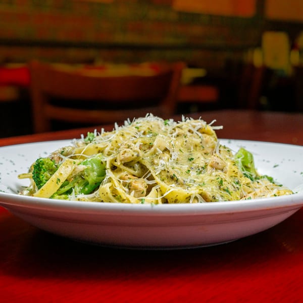 Pasta with pesto sauce, broccoli, and grated cheese in a white bowl on a red table.