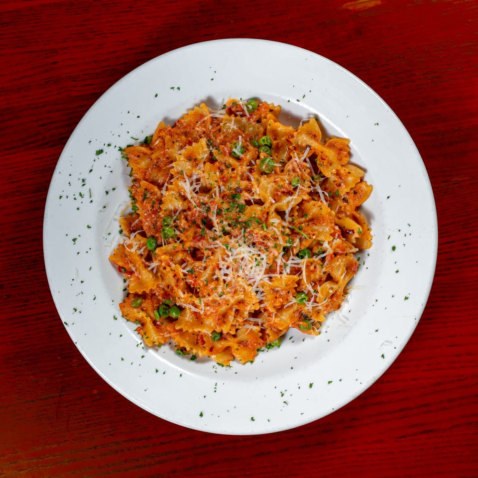 Farfalle pasta with red sauce, green peas, grated cheese, and parsley on a white plate.