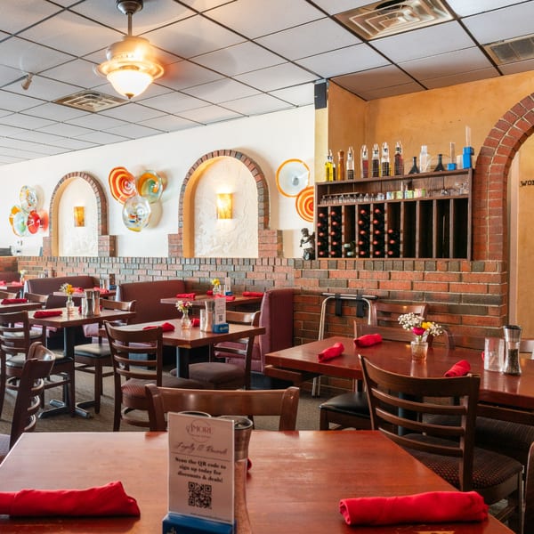 An empty Italian restaurant dining room with brick arches, wooden tables, and red napkins.