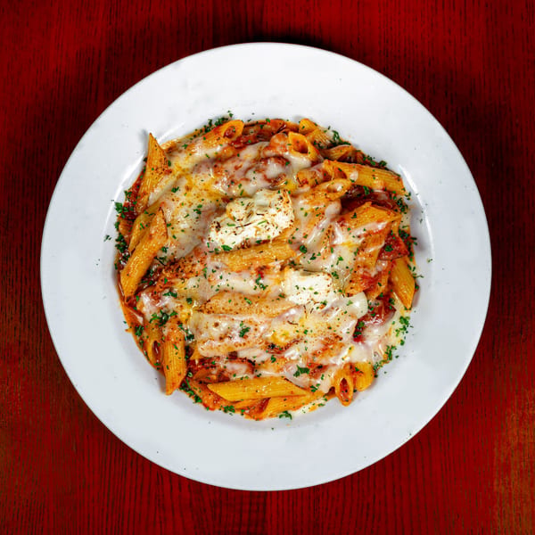 Baked penne pasta with melted cheese, tomato sauce, and parsley on a white plate.