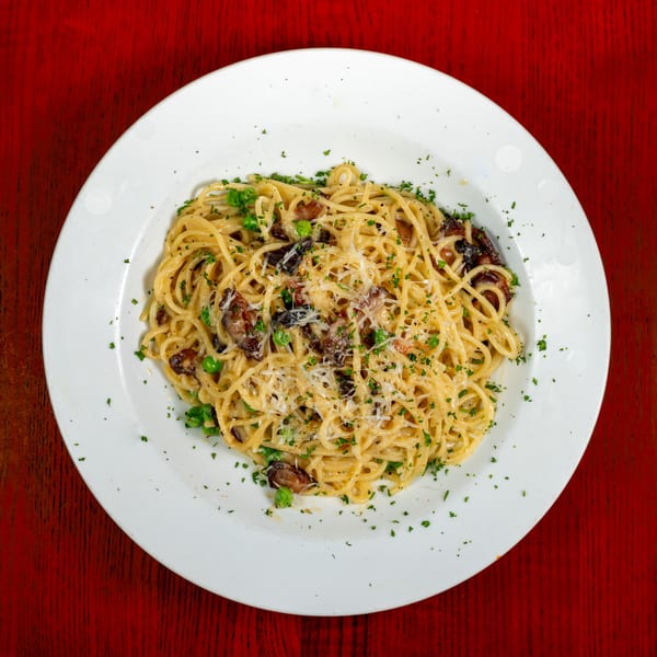 Overhead view of spaghetti with mushrooms, peas, and grated cheese on a white plate.