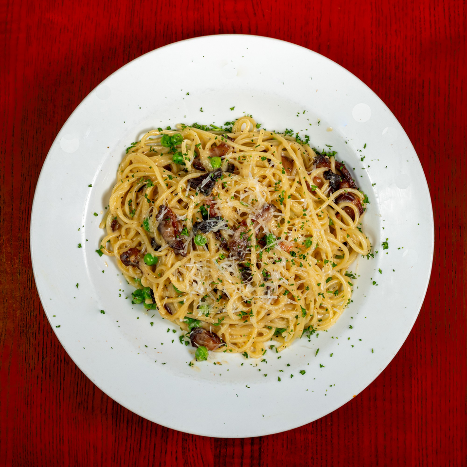 Overhead view of spaghetti with mushrooms, peas, and grated cheese on a white plate.