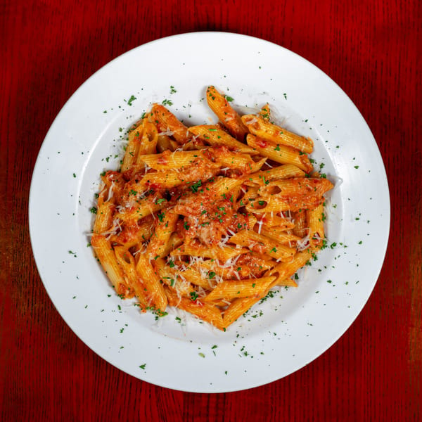 Penne pasta with red sauce, parmesan cheese, and parsley on a white plate.