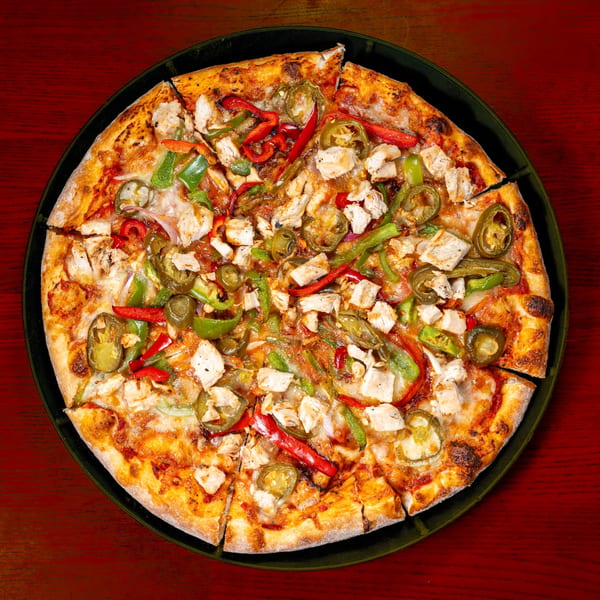 A whole chicken pizza with red and green peppers, and jalapeños, on a dark plate.