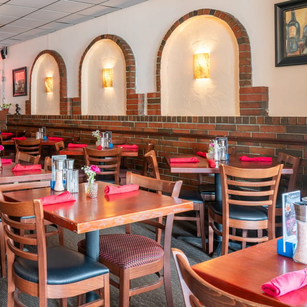 Restaurant dining room with wooden tables, red napkins, and brick archways with sconce lighting.